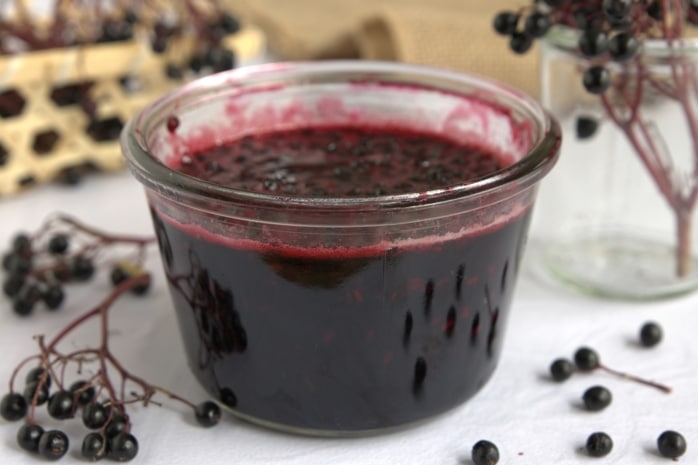 Holunderbeerenmarmelade im Glas mit frischen Holunderbeeren