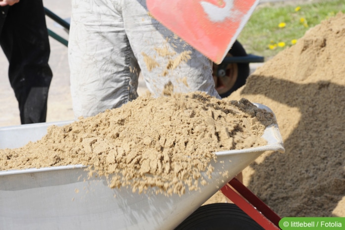 Sand mit Schaufel in Schubkarre füllen