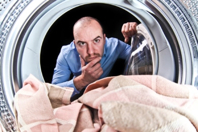 Mann schaut skeptisch in die Waschmaschine
